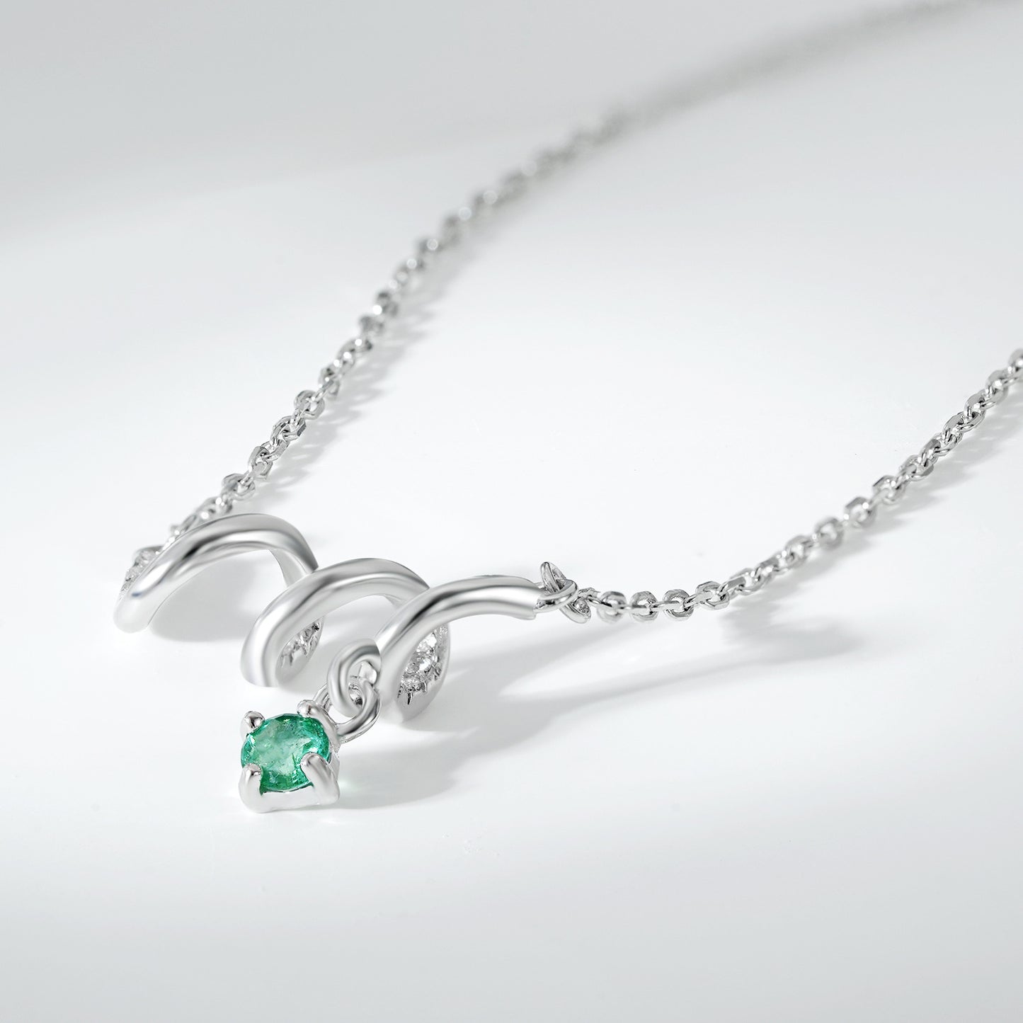 Silver necklace with a green gemstone on a light gray background