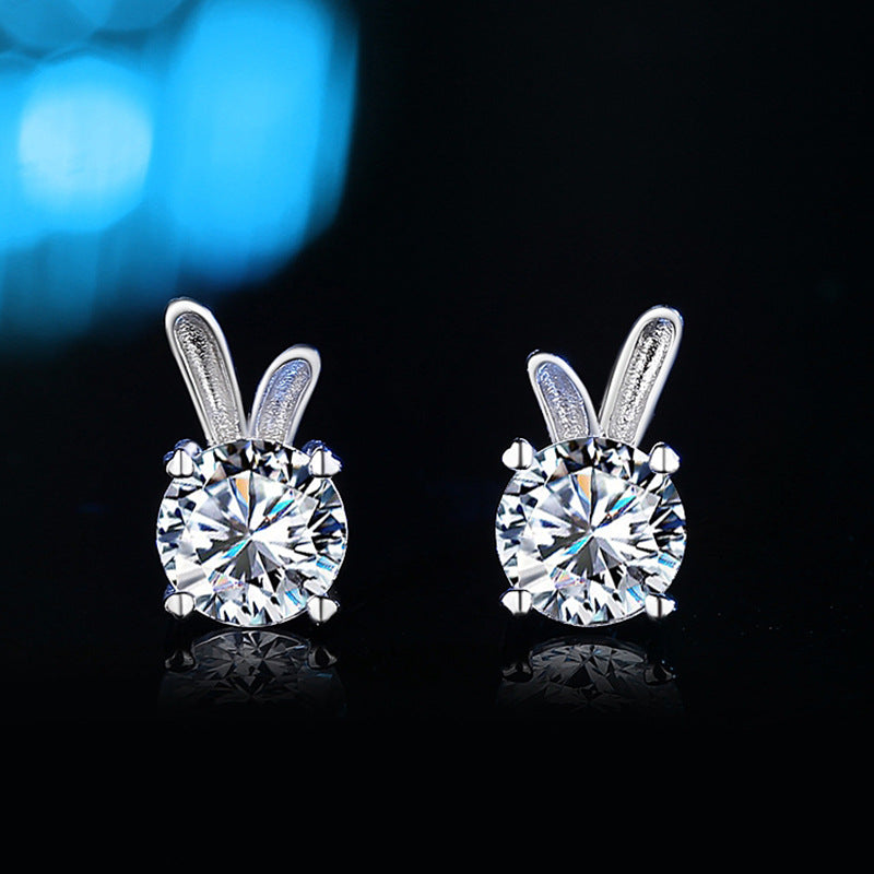 Silver bunny ear-shaped earrings with clear gemstones on a black background