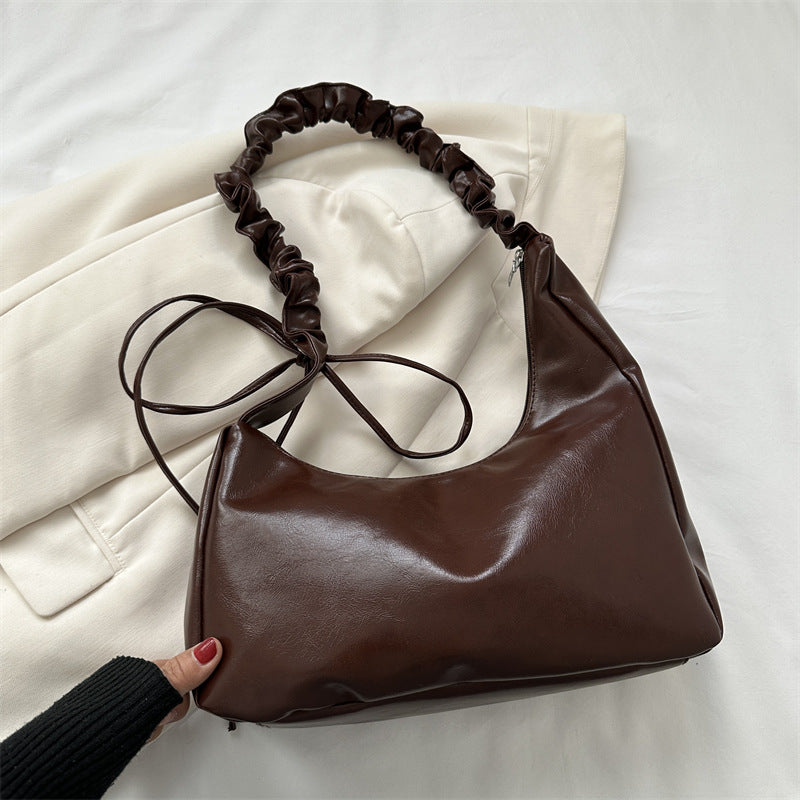 Brown leather handbag with ruched handle on a white surface