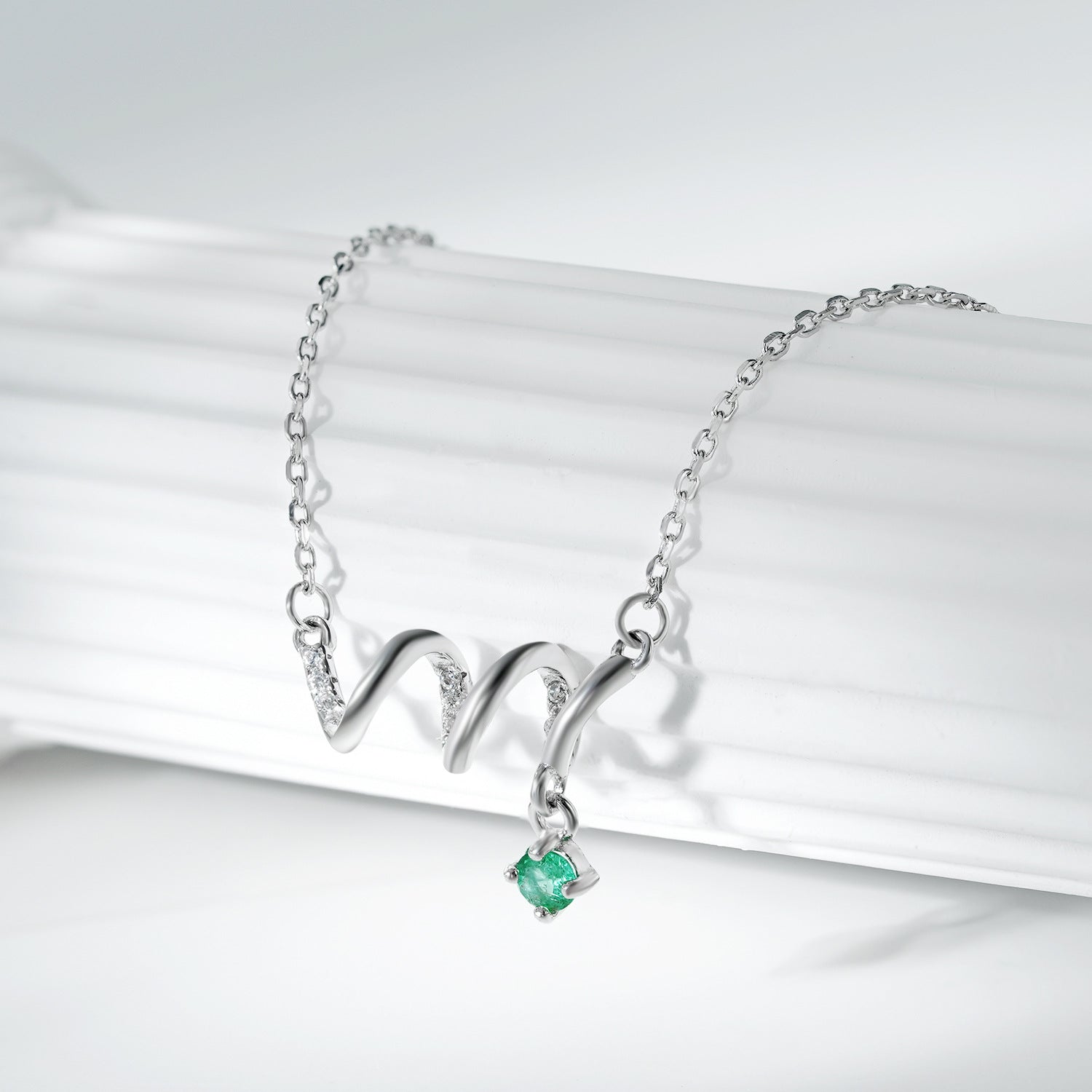 Silver necklace with a green gemstone pendant on a white background