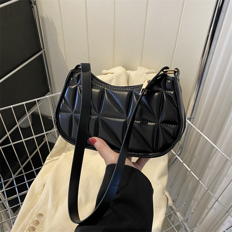 Black quilted handbag held by a person against a tiled wall background