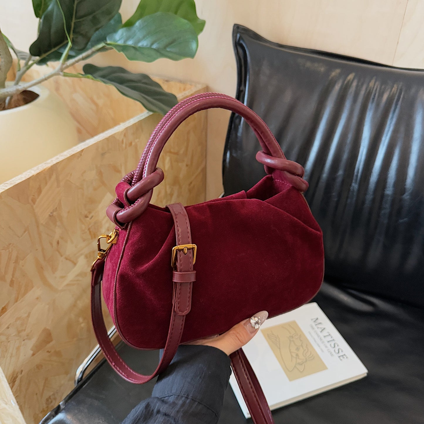 Red handbag held by a person with a book and plant in the background