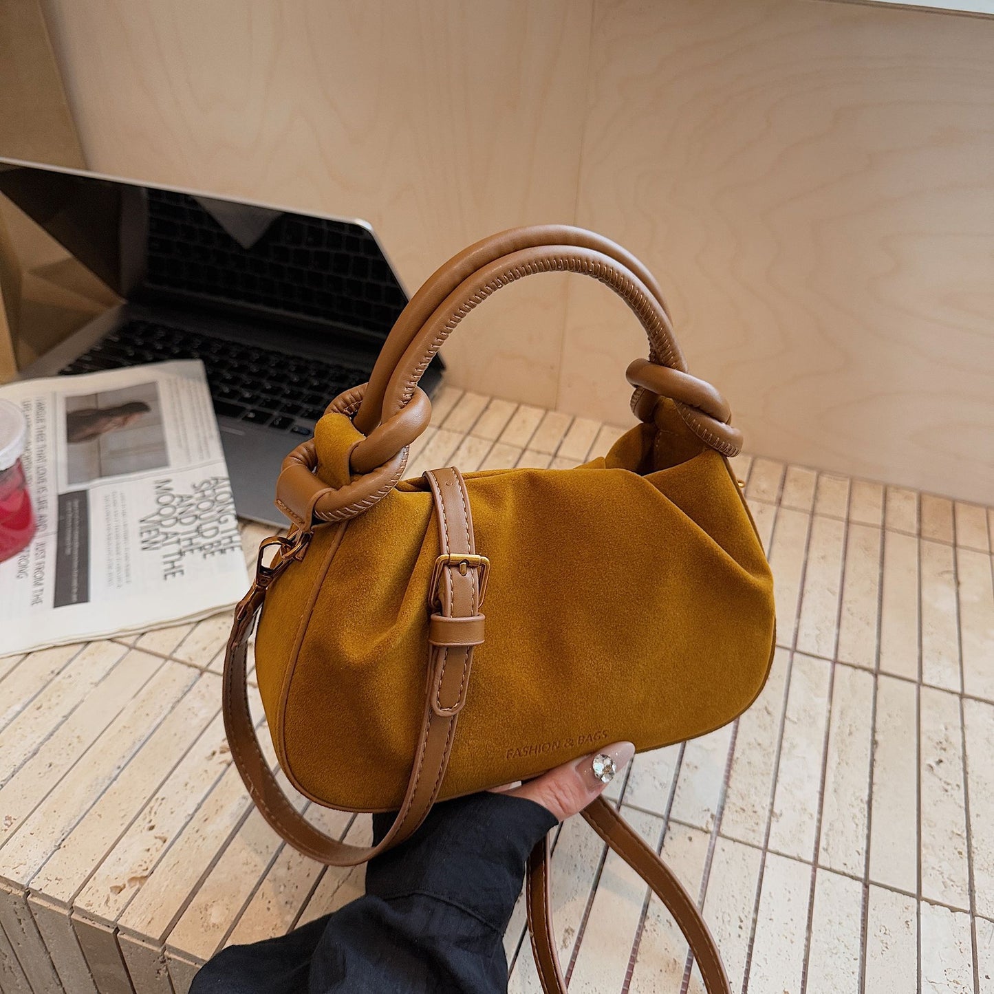 Mustard yellow handbag with knotted handle held by a person on a wooden surface.